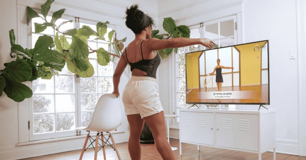 אישה לומדת לרקוד בלט קלאסי בתוכנית דיגיטלית על הטלויזיה בסלון
